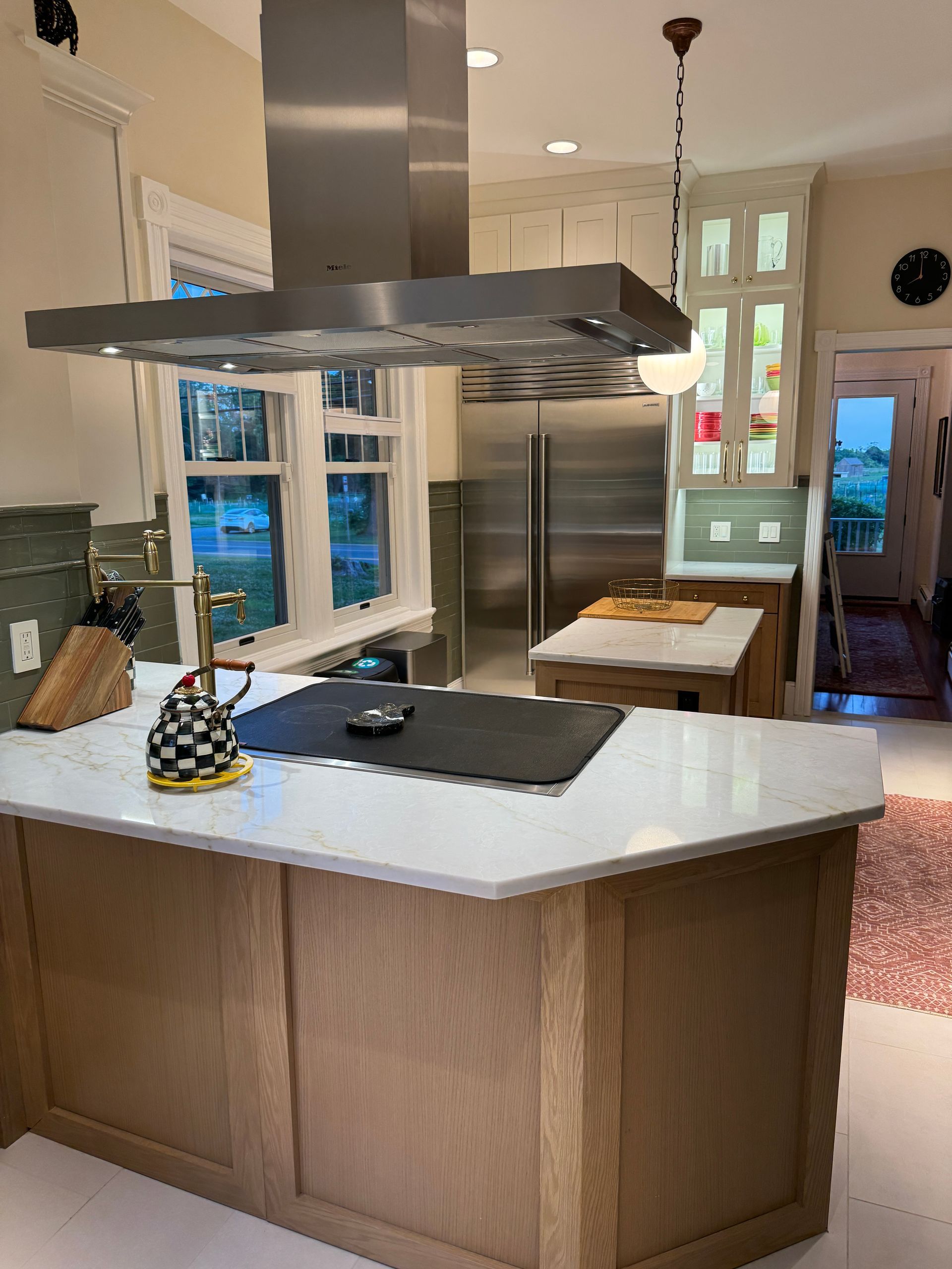 Modern kitchen with a white island, stainless range hood, pendant lights, and glass doors to a patio.