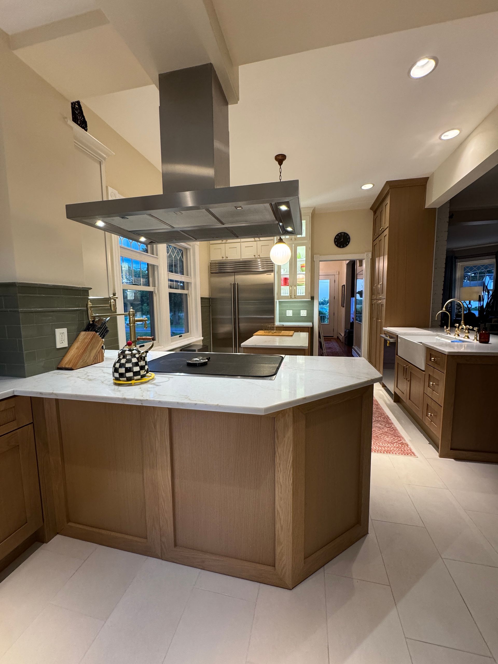 Modern kitchen with large island, stainless range hood, and wood cabinetry under recessed lights
