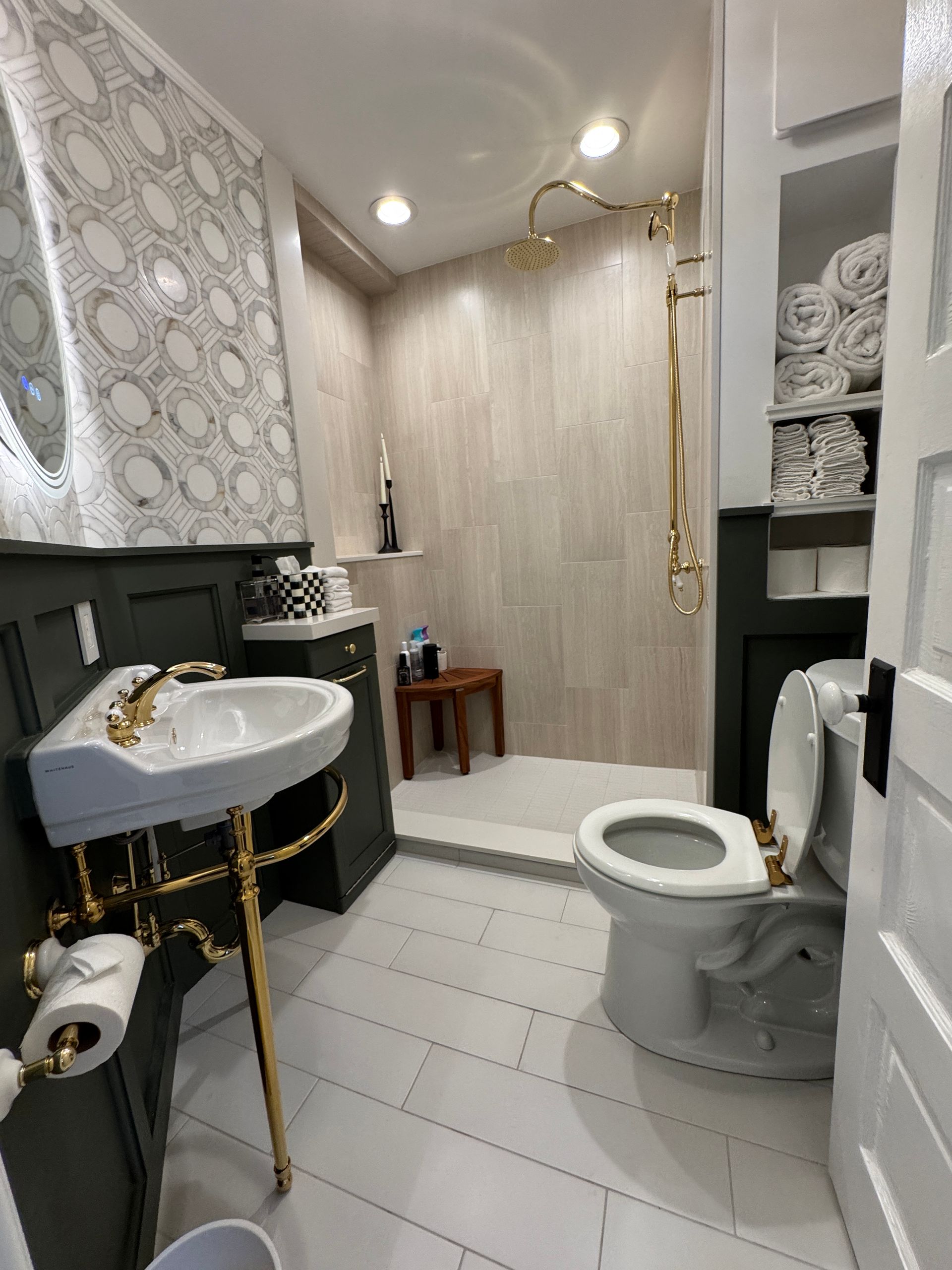 Small bathroom with sink, toilet, shower, and folded towels in a compact, modern space.