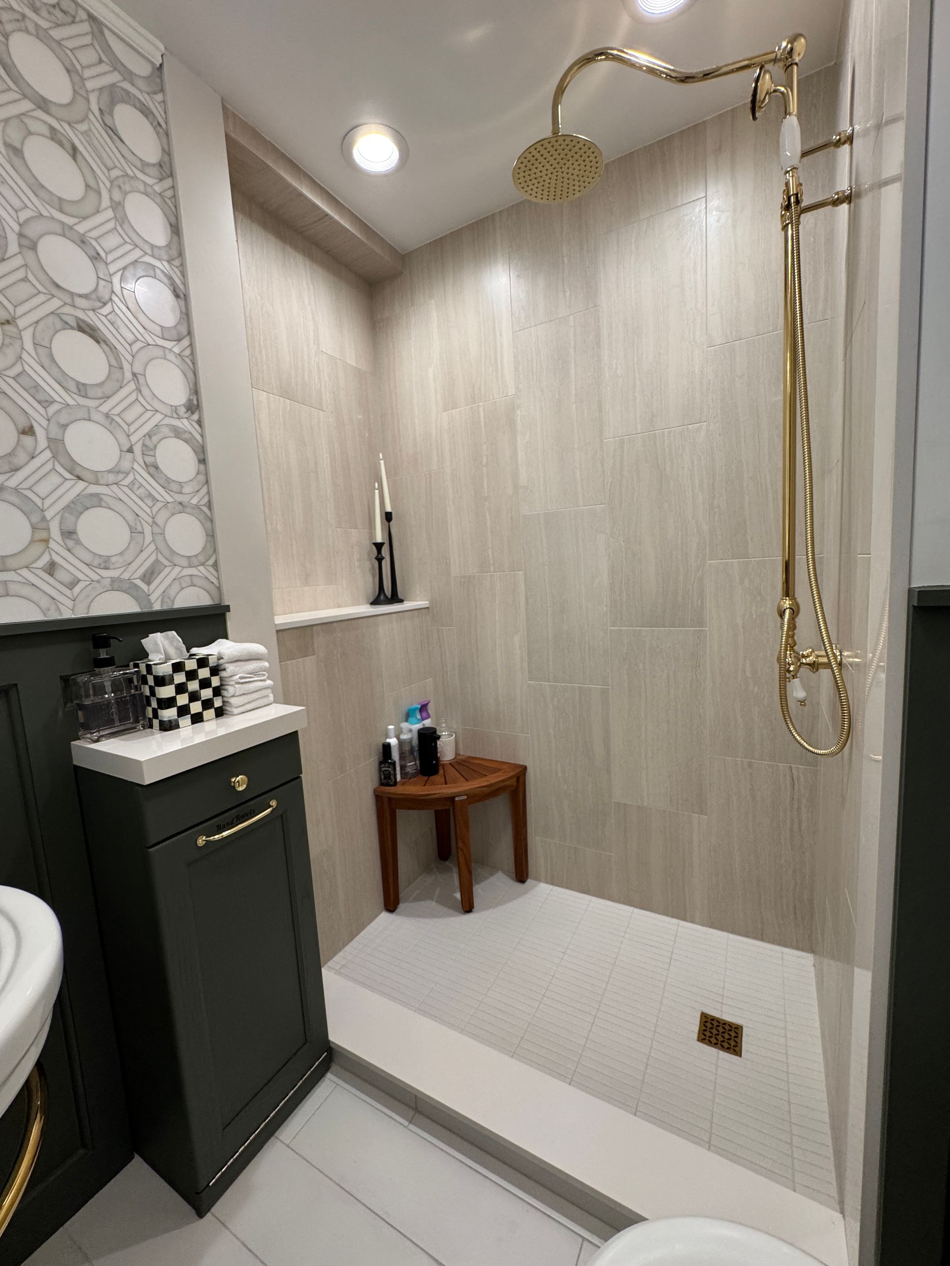 Luxury bathroom shower with gold fixtures, gray tile walls, and a built-in bench with toiletries