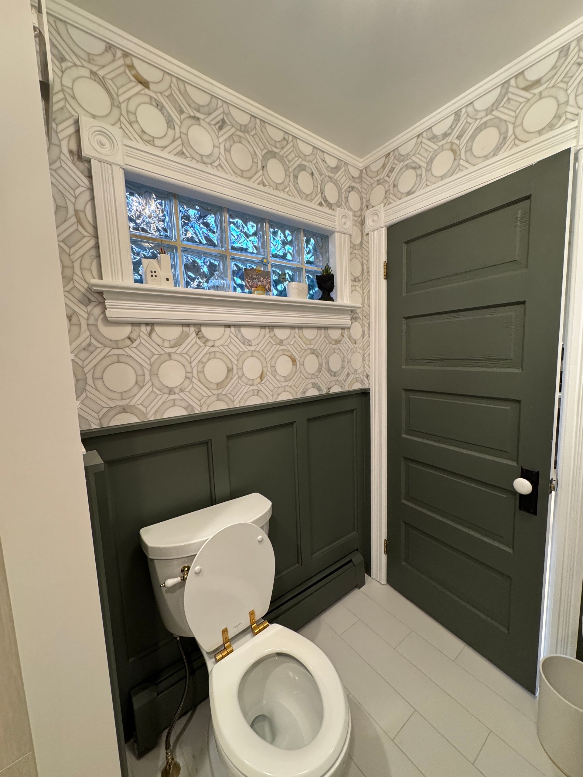 Small bathroom with a toilet, dark green wainscoting, patterned wallpaper, and a matching green door.