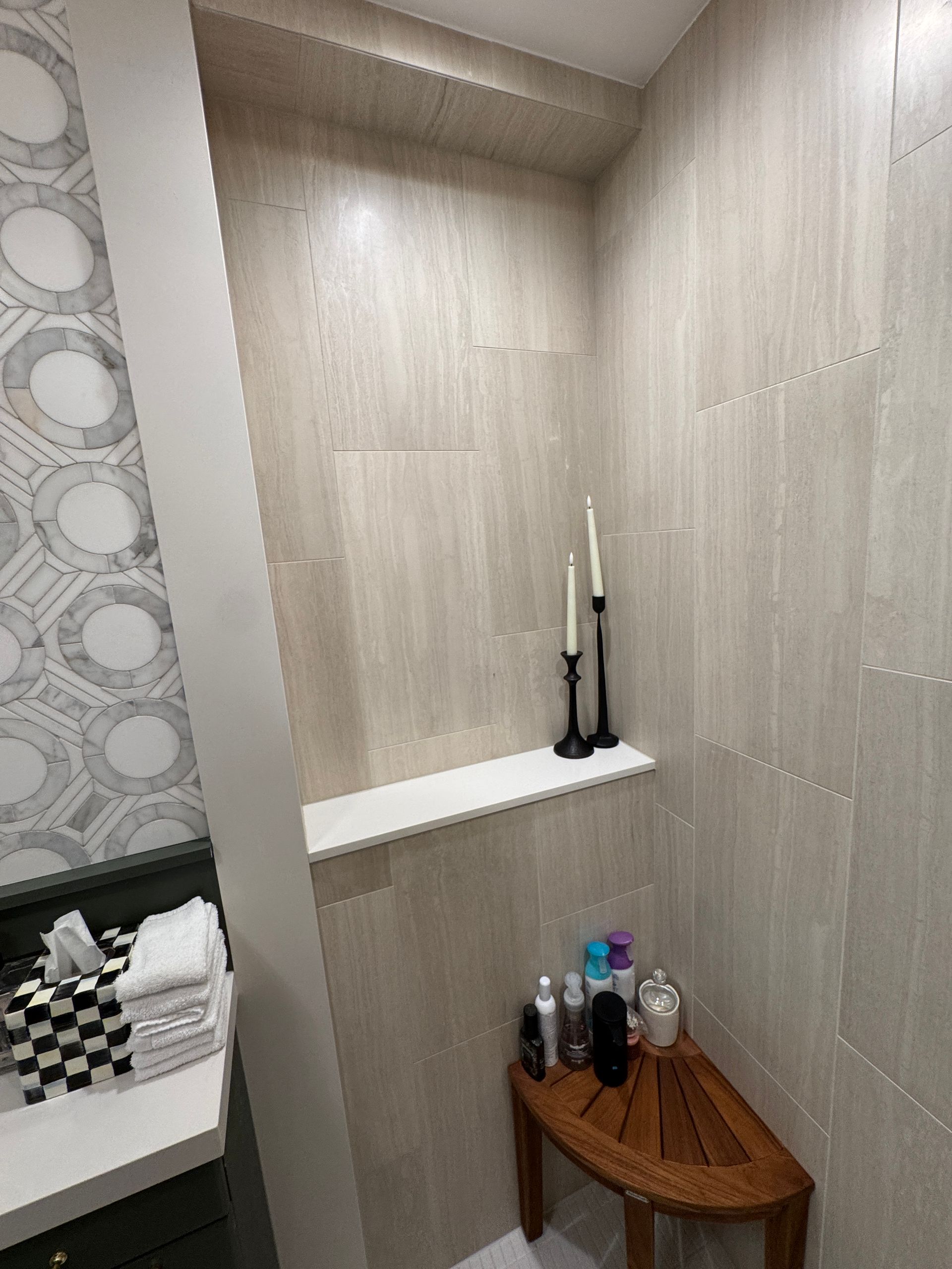 Bathroom alcove with white shelf, black decor, and a small wooden table holding bottles.