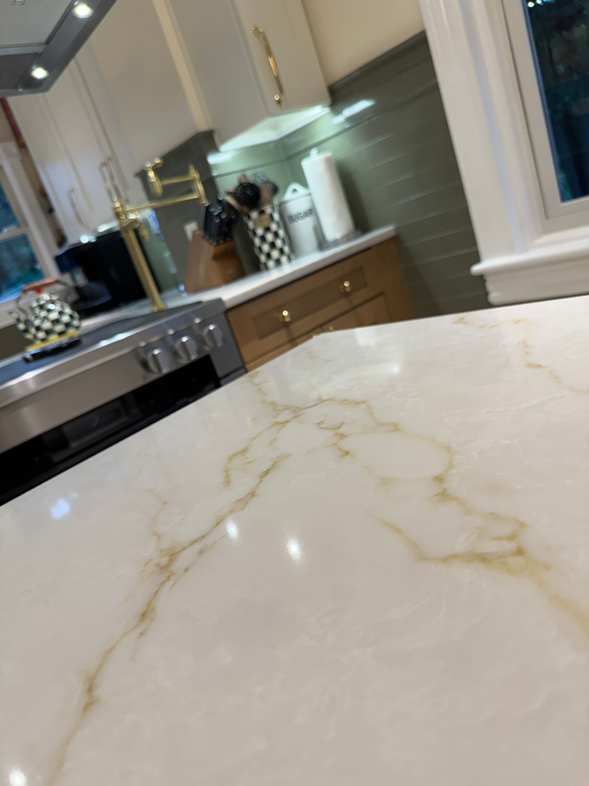 Modern kitchen with white marble countertop, stainless stove, wood cabinets, and a windowed backsplash.