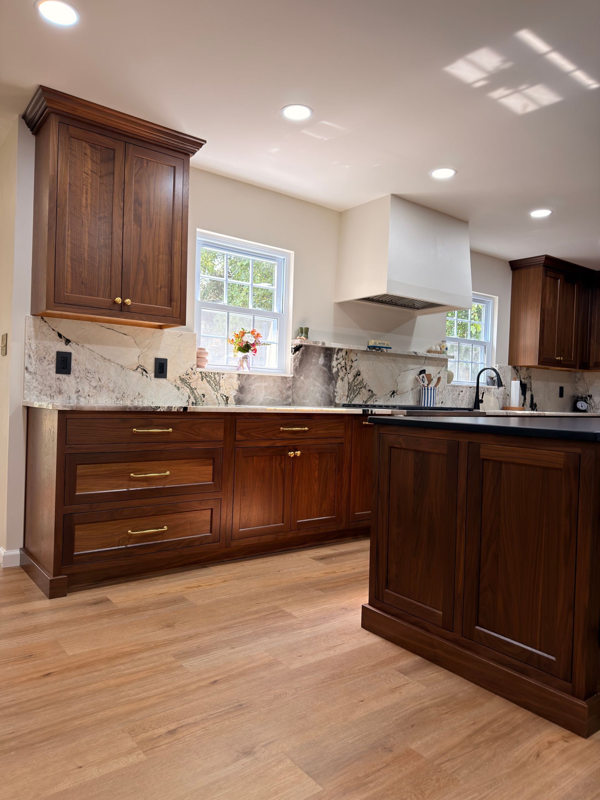 Bright kitchen with dark wood cabinets, black countertops, stainless range hood, and hardwood floors