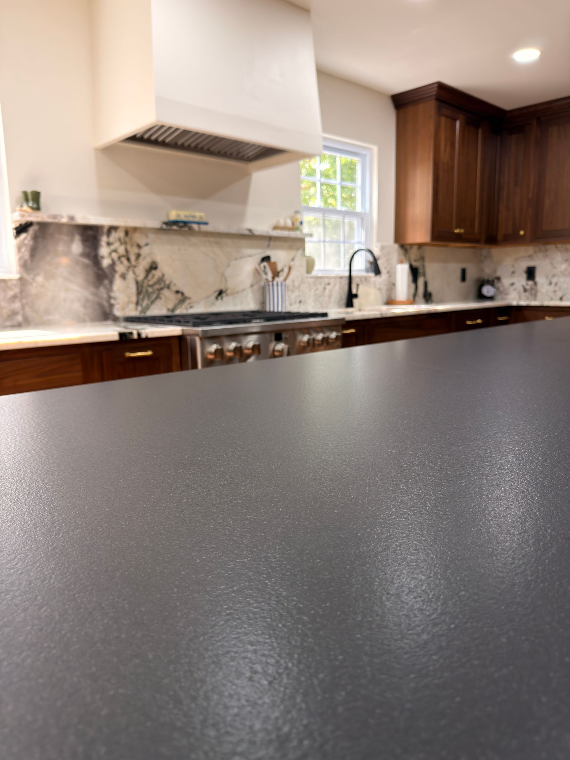 Modern kitchen with dark speckled countertop, wood cabinets, and stainless-steel range hood