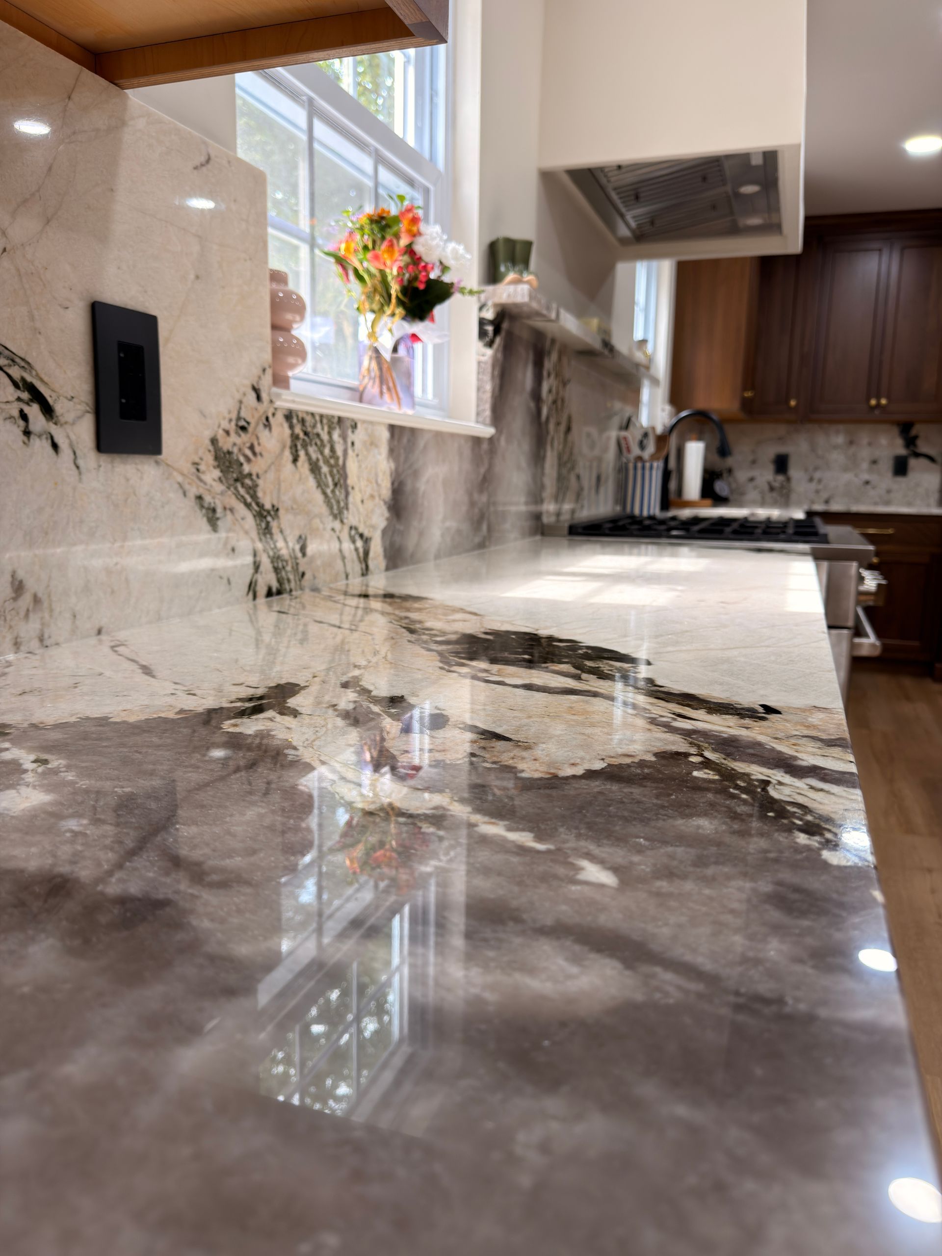 Shiny granite kitchen countertop with window, flowers, and dark wood cabinets.