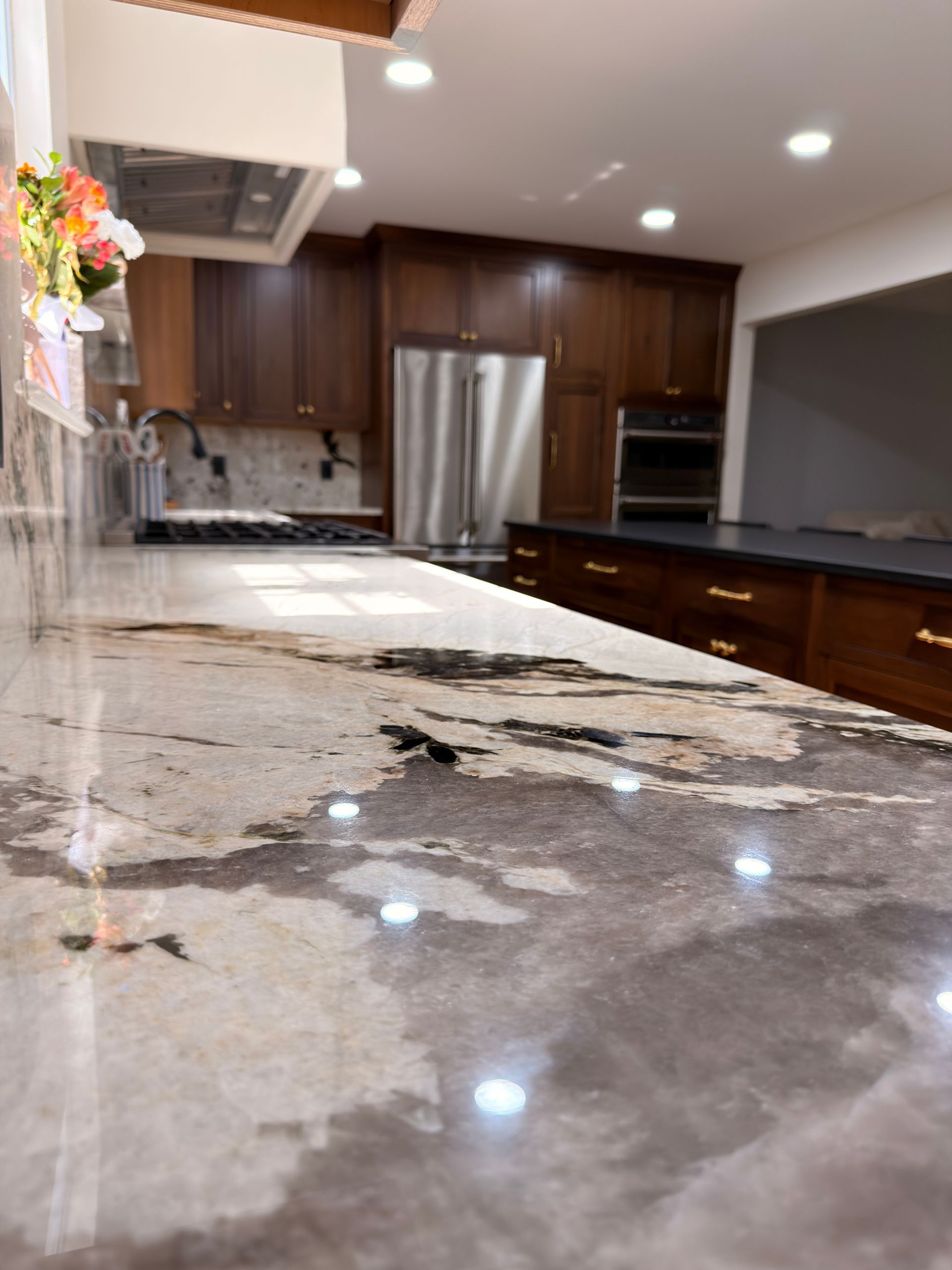 Modern kitchen with a large polished marble island, dark wood cabinets, and stainless steel appliances.