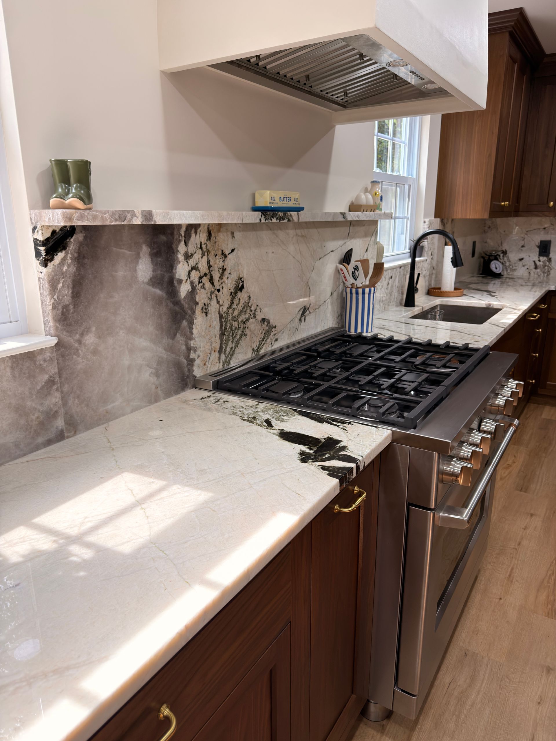 Modern kitchen with marble countertops, gas range, stainless oven, sink, and wood cabinets.