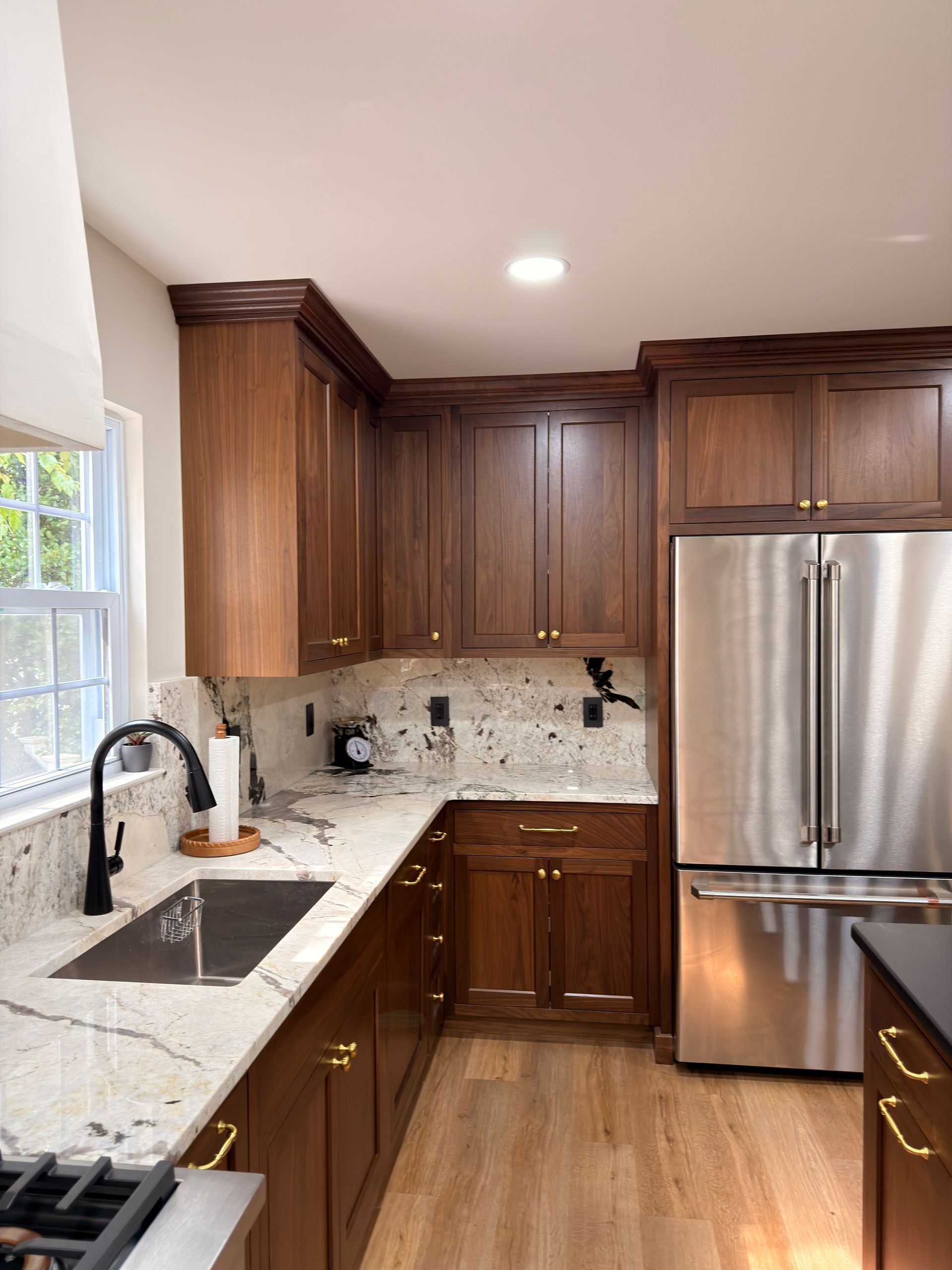 Modern kitchen with dark wood cabinets, marble counters, stainless steel fridge, and a large window by the sink