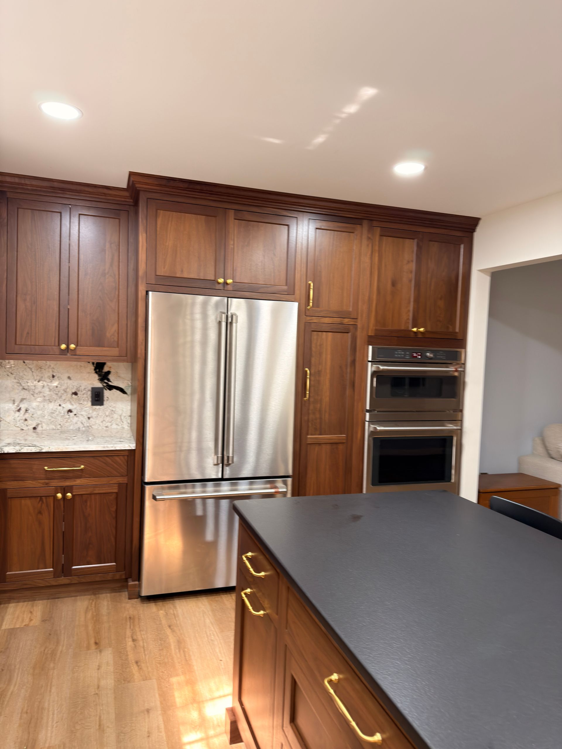 Modern kitchen with dark wood cabinets, stainless steel fridge, built-in oven, and dark island countertop.