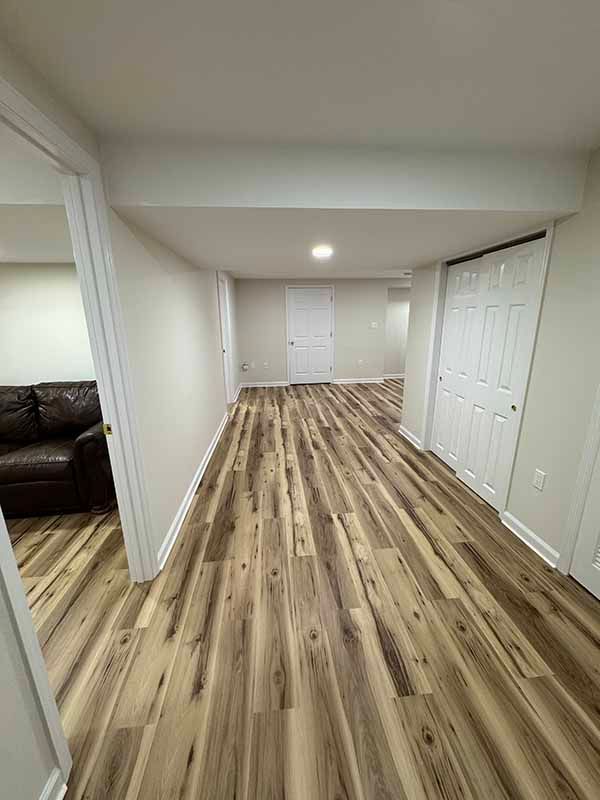 Interior view of a finished basement with wood-look flooring, white walls, and a hallway.