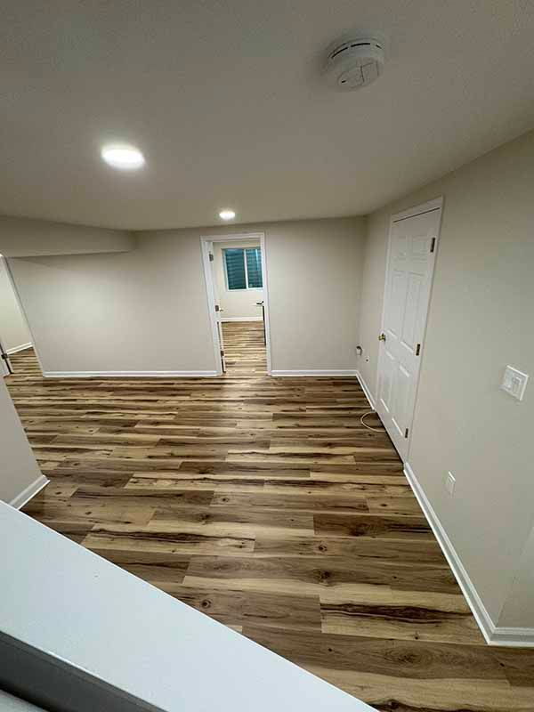 Empty room with wood-look flooring, white walls, two doorways, and a smoke detector on the ceiling.