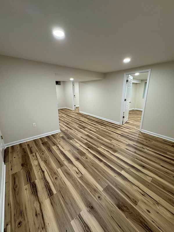 Empty room with wood-look flooring, white walls, recessed ceiling lights, and two doorways.