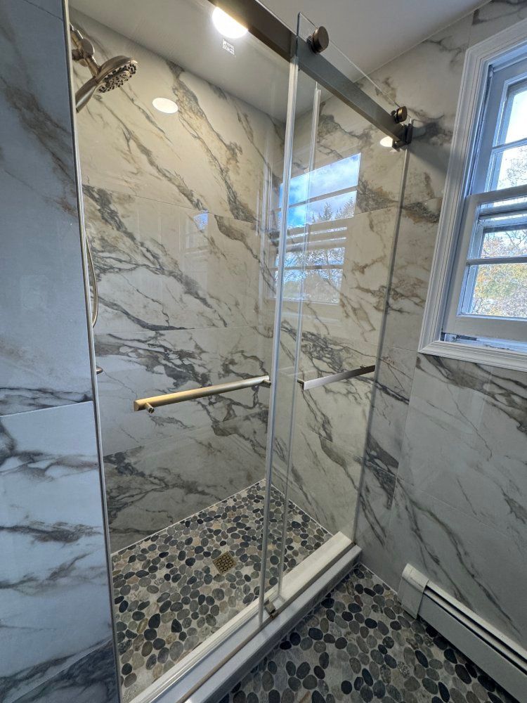 Modern bathroom with glass shower door, marble tile walls, and pebble floor.