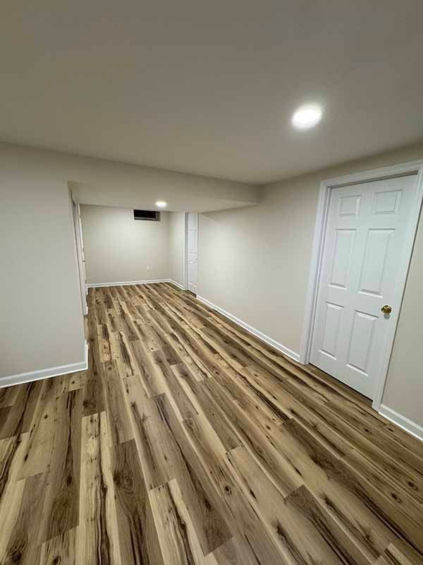 Empty room with wood-look flooring, white walls, and a closed white door.