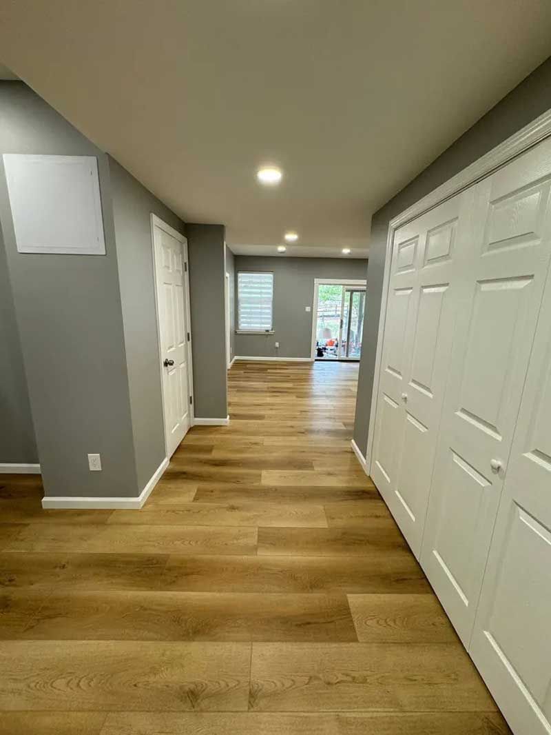 Hallway with wood-look flooring, gray walls, white doors, and recessed ceiling lights.