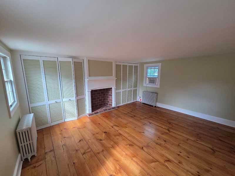 Empty room with wooden floor, fireplace, and built-in closet.