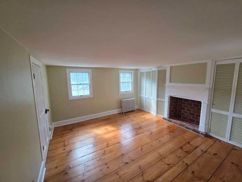 Empty room with wide wood floors, beige walls, a window, fireplace, and white louvered closets