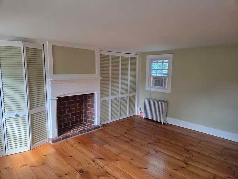 Empty room with a fireplace, wooden floors, and a window with a radiator.