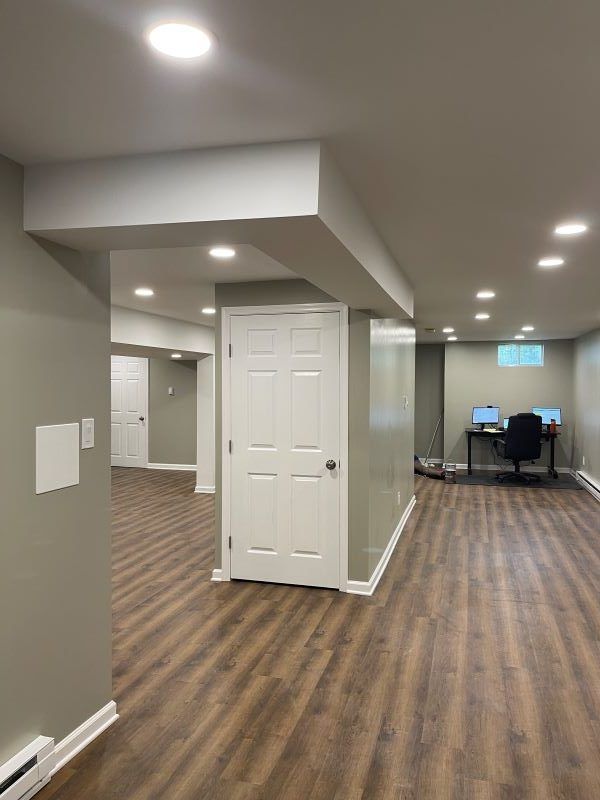 Finished basement with wood-look flooring, recessed lighting, and a workspace with computers.