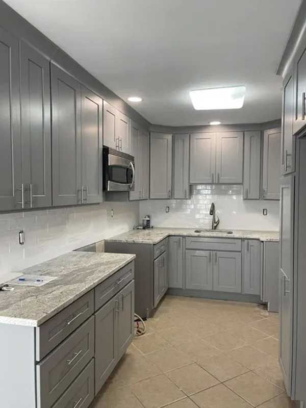 Gray kitchen cabinets with a light countertop and tile backsplash.