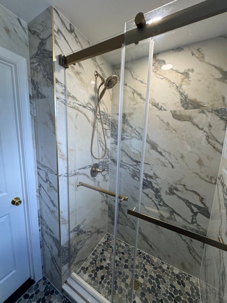 Shower with marble tile walls, sliding glass doors, and pebble floor.