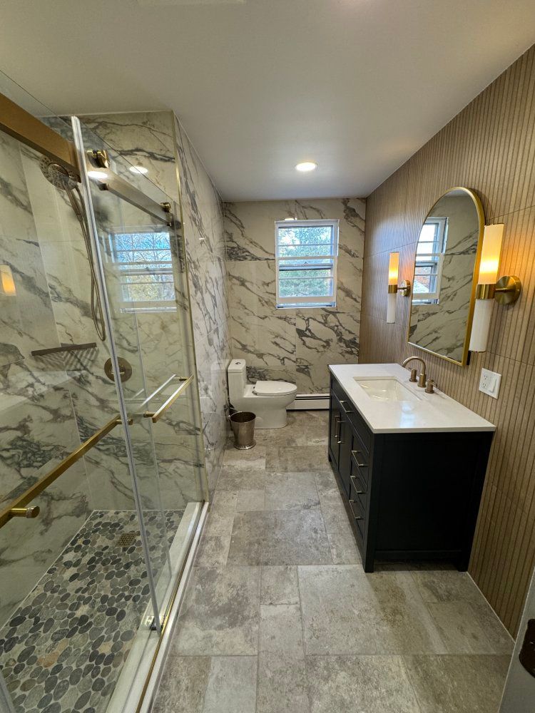 Modern bathroom with marble shower, black vanity, and gold accents.