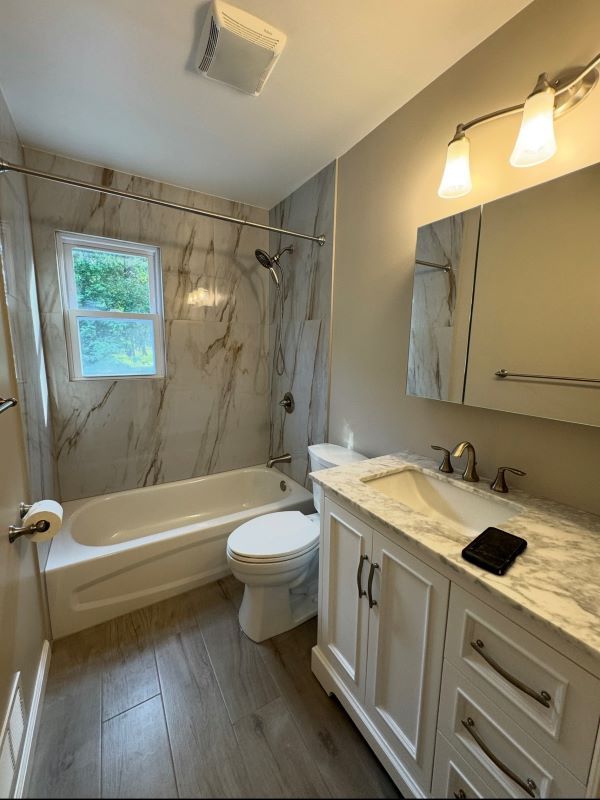 Bathroom with white tub, marble-look tile, white vanity, silver fixtures, and wood-look flooring.