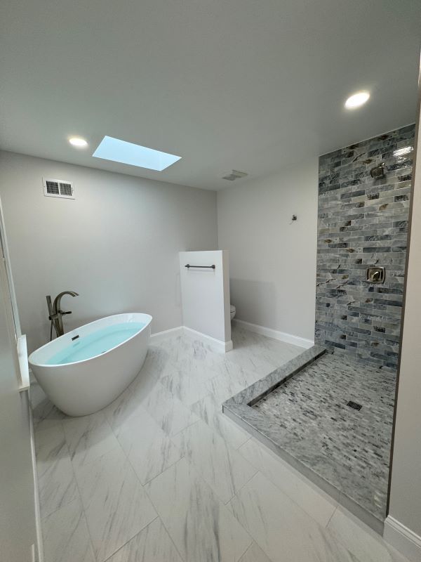 Modern bathroom with white soaking tub, walk-in shower, marble floors, and accent tile.