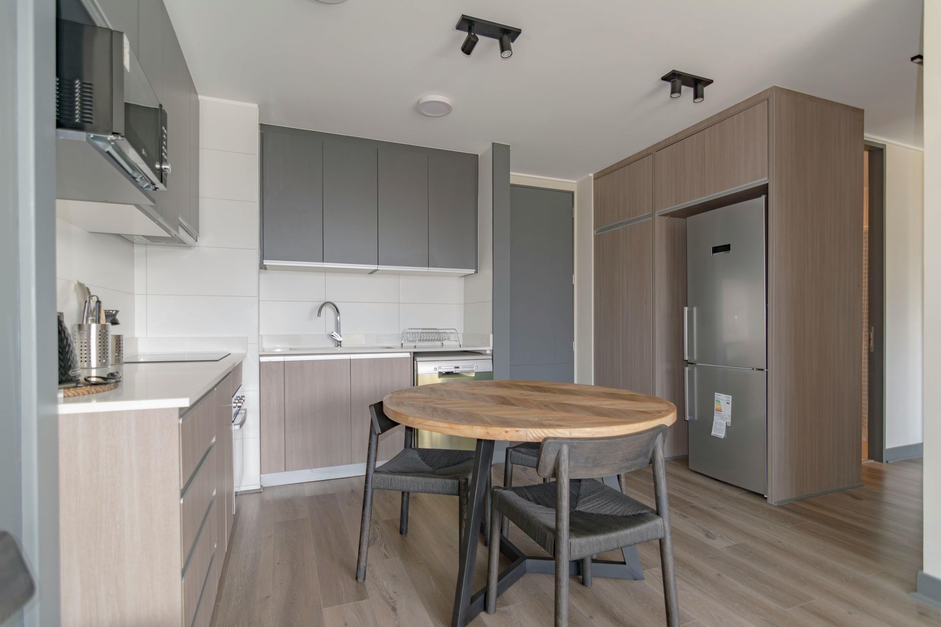 Modern kitchen with gray cabinets, wood flooring, round table, and stainless steel refrigerator