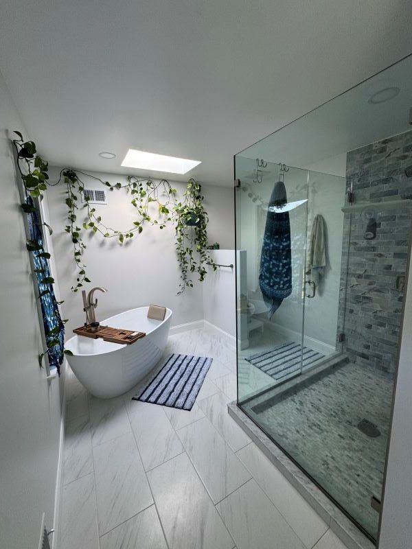 Bright modern bathroom with freestanding tub, glass shower, white tile, and hanging plants.