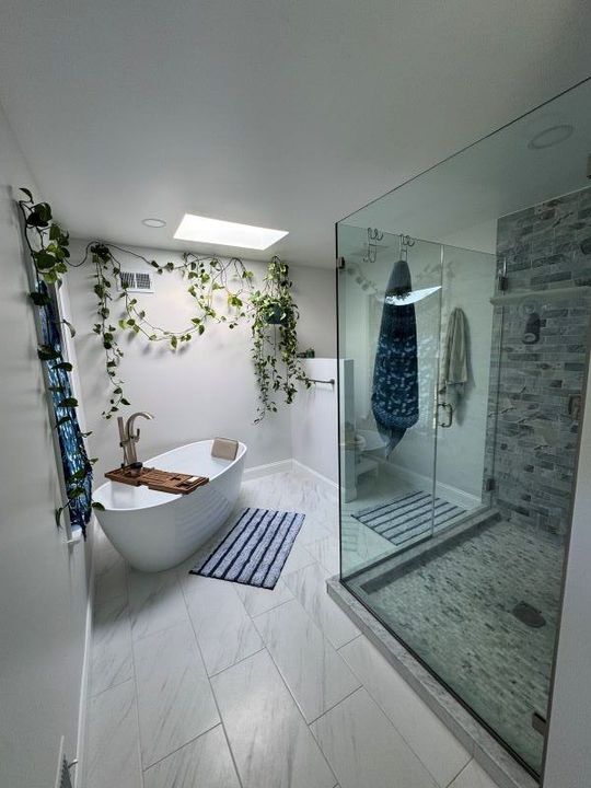 Modern bathroom with white tub, glass shower, and trailing greenery.
