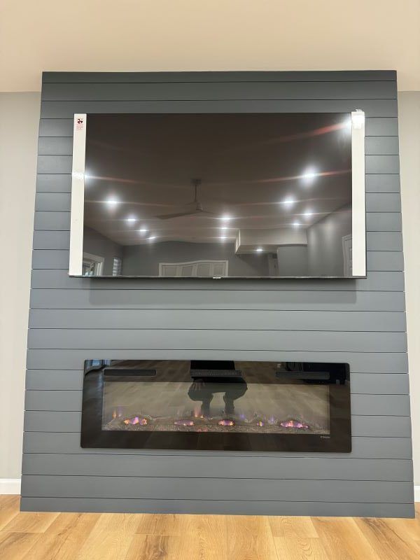 TV mounted above an electric fireplace on a gray shiplap wall.