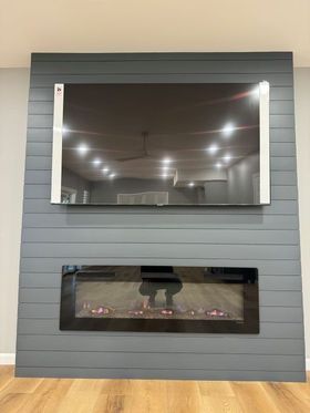 Grey shiplap wall with mounted TV above a fireplace. Room has wood flooring.