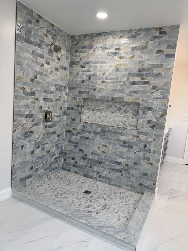 Tiled shower with blue and gray brick-style wall tiles, a stone floor, and a recessed shelf.