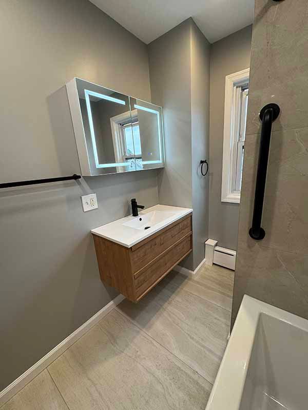 Modern bathroom with floating wooden vanity, lighted mirror, and grab bar.