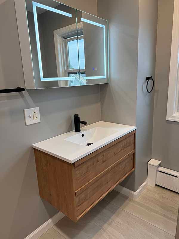 Modern bathroom with a wooden floating vanity, lit mirror, and black faucet.