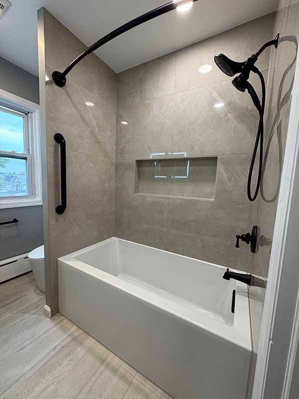 Modern bathroom with gray tiled walls, a white tub, and black fixtures.