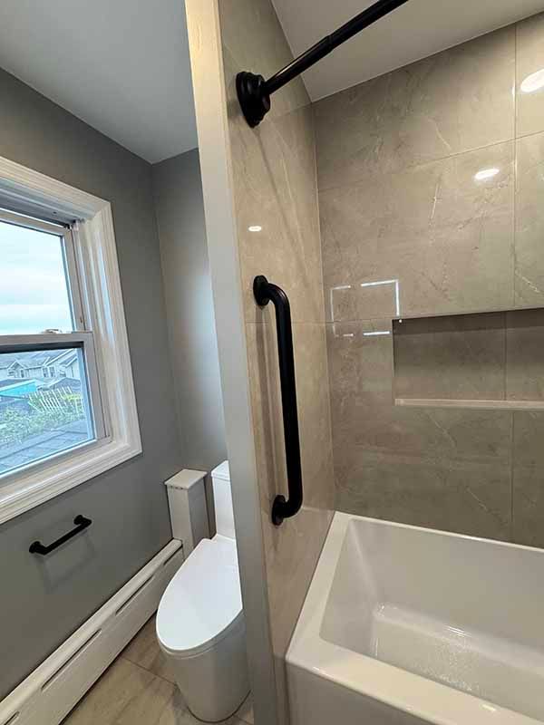 Bathroom with a white toilet, gray walls, and a black grab bar near the bathtub.