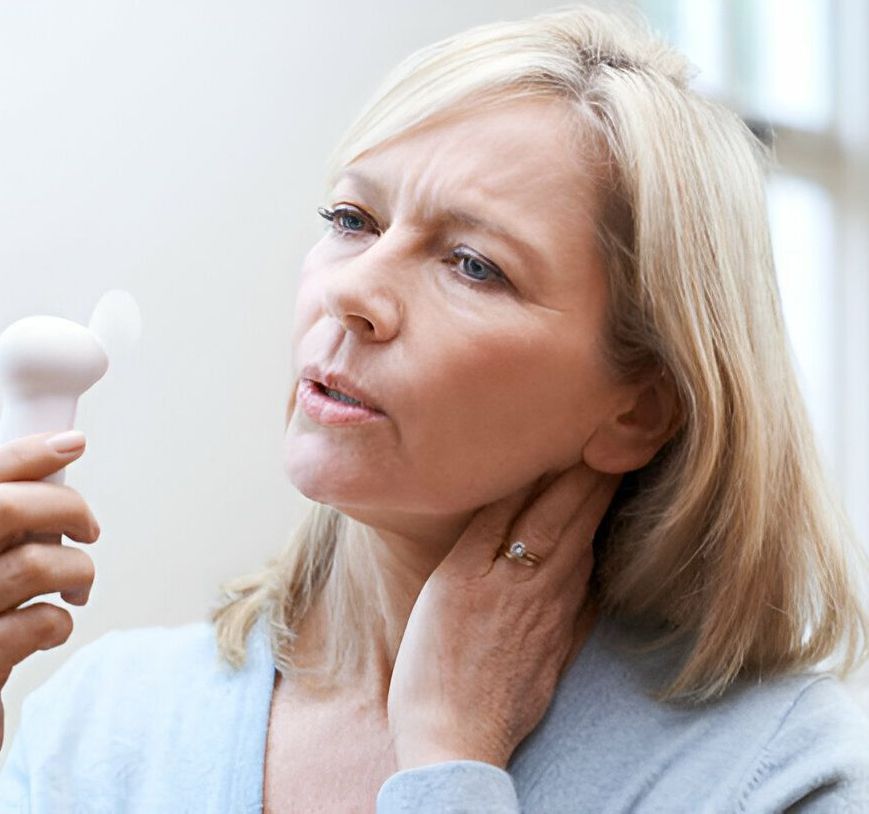 Woman holding a fan, touching her neck, and looking uncomfortable.