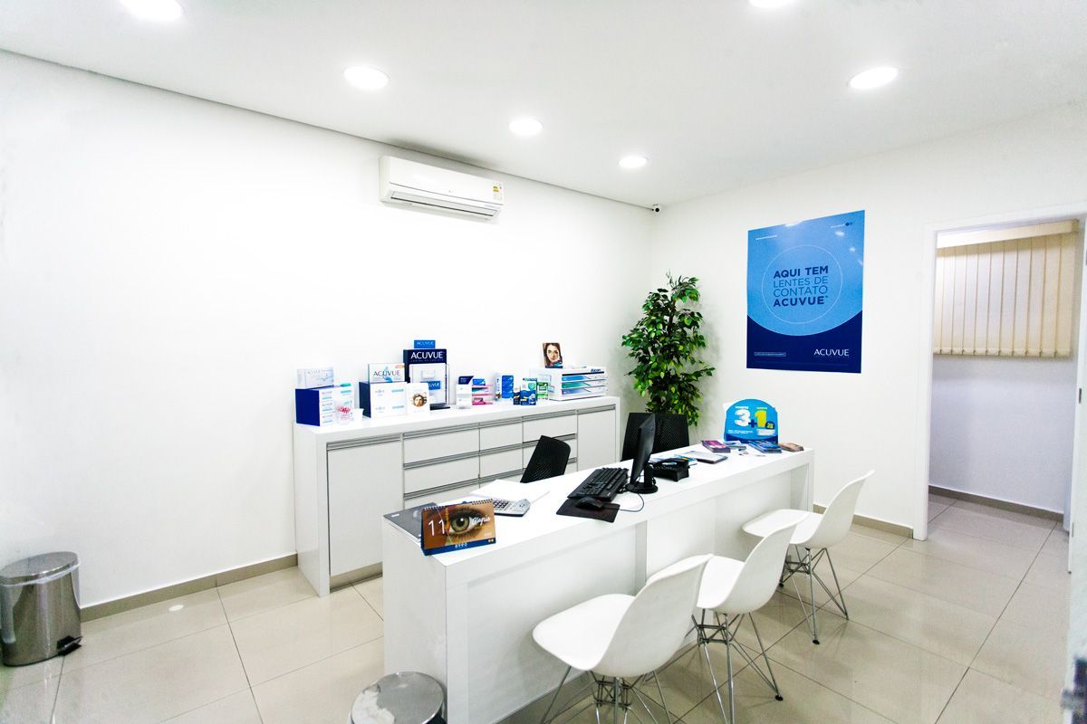 Um escritório luminoso e minimalista com mesa, cadeiras e estantes brancas, além de uma placa informativa azul na parede.