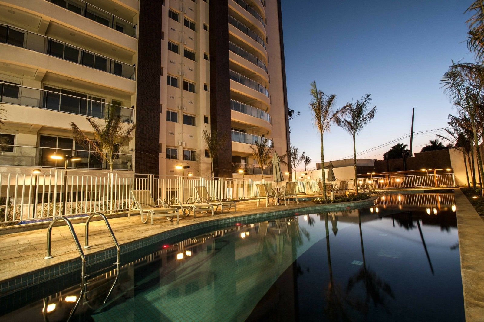 Prédio de apartamentos moderno com piscina que reflete o céu noturno e iluminação externa.