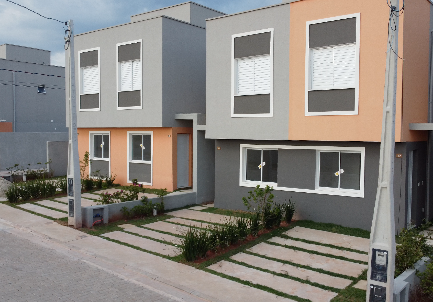 Duas casas geminadas modernas de dois andares com fachadas em tons de cinza e pêssego, janelas com molduras brancas e entradas de automóveis pavimentadas.