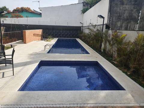 Duas piscinas retangulares com fundo de azulejos azul-escuros, inseridas num pátio de concreto de cor clara.