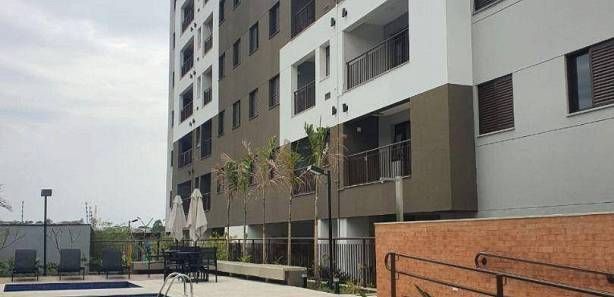 Um prédio de apartamentos de vários andares com fachada branca e marrom, adjacente a uma área de pátio com palmeiras e lounge com piscina.