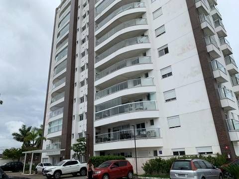 Um prédio residencial de vários andares com varandas curvas brancas, detalhes verticais em marrom escuro e carros estacionados.
