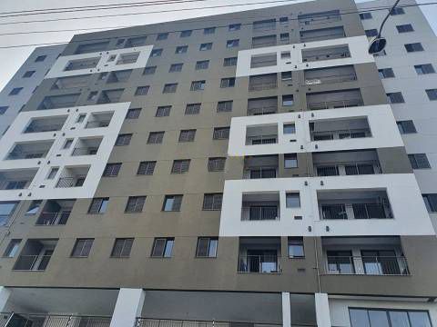 Um moderno edifício de apartamentos de vários andares com fachada cinza, apresentando varandas recuadas com detalhes em branco e janelas em forma de grade.