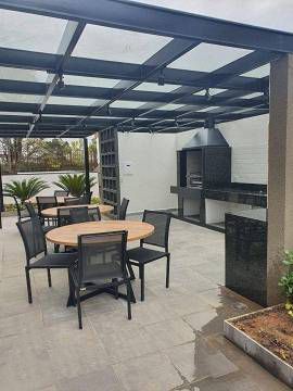 Um pátio externo com área de estar coberta, mesa de jantar e uma moderna churrasqueira embutida.