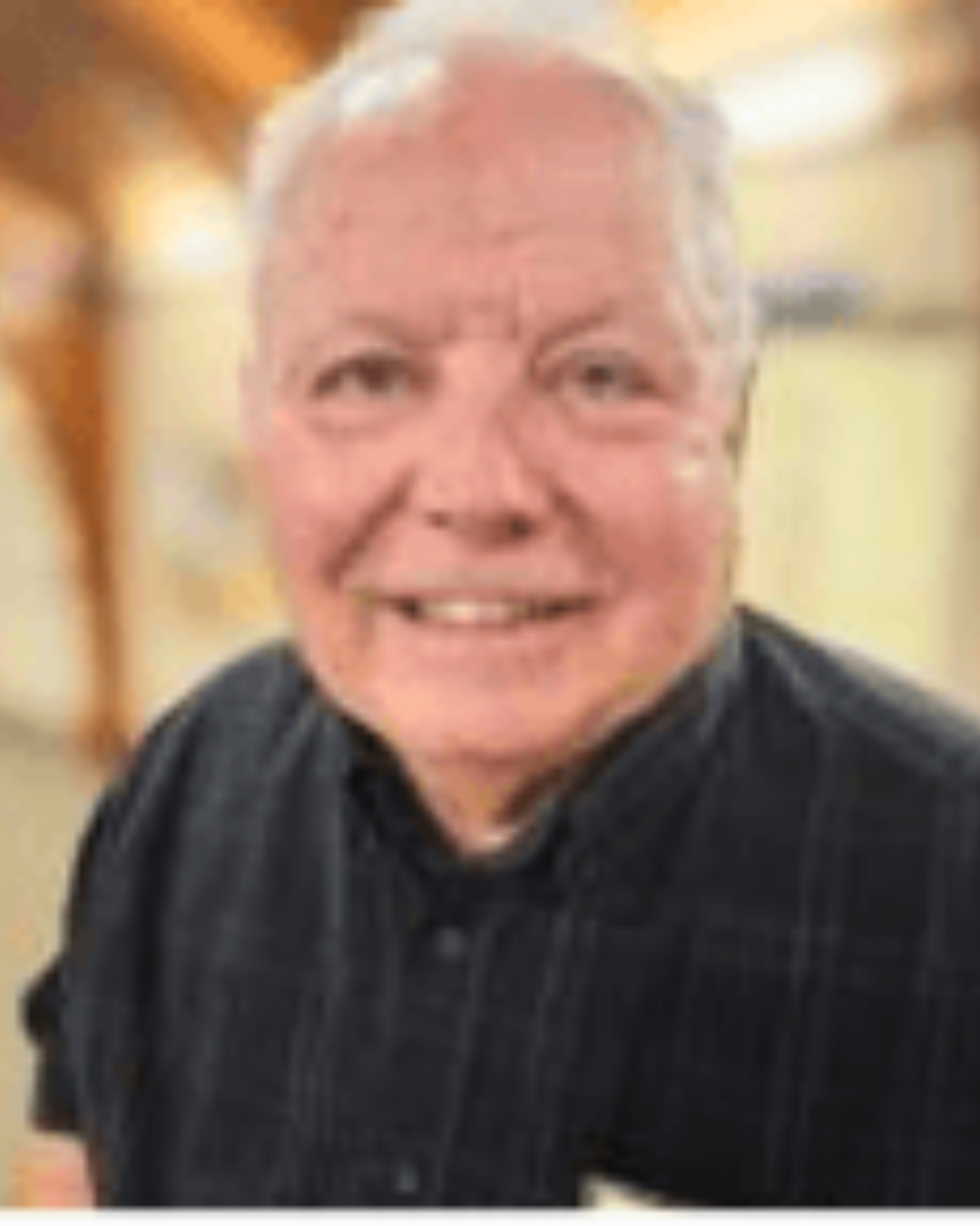 Smiling man in a dark shirt indoors, with a softly blurred background
