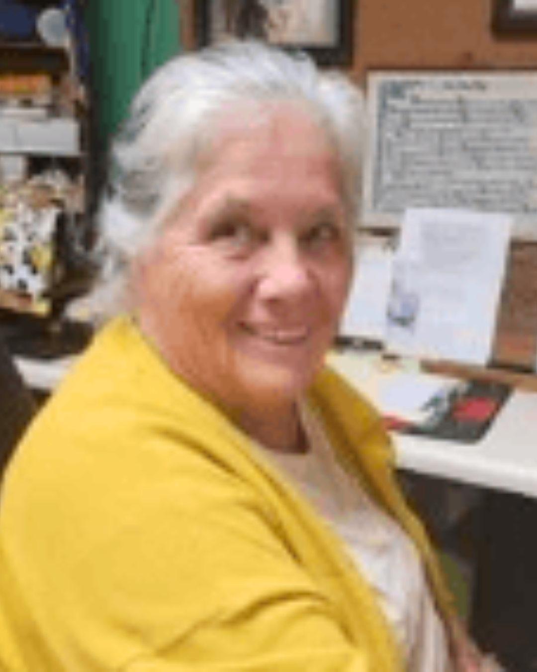 Smiling woman in a yellow cardigan seated at a desk in an office or workspace